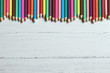Colored pencils border on a wooden background, with copy space