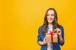 © denis_vermenko - Smiling young beautiful woman holds red gift box. Isolated over yellow background. Studio.