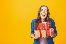 Young Smiling Model Hold Gift Box. Woman Isolated On Yellow Background.