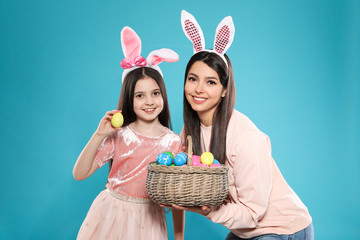 Sticker - Mother and daughter in bunny ears headbands with basket of Easter eggs on color background