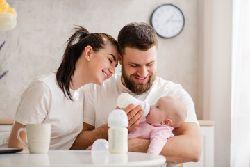 Happy young couple feeding infant from bottle