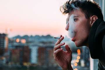 Wall Mural - Young man smoking a cigarette on the balcony in sunset