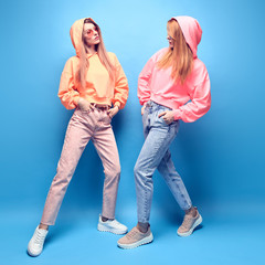 Fashion. Two hipster Girl in trendy colorful neon Outfit Fooling Around in Studio. Young Tomboy Friends Having Fun relax. Shapely Woman with fashionable makeup. Funny art neon style, full-length