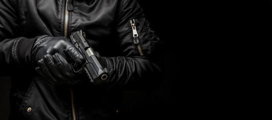 a man in a black jacket and black gloves holding a gun on a dark back