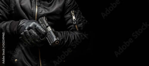 Fotografía a man in a black jacket and black gloves holding a gun on a dark back