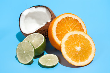 Wall Mural - Fresh juicy orange, coconut and green lime isolated on blue background. Concept of Healthy eating and dieting. Travel and holiday concept