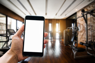 A man hand holding smart phone device in the fitness room view background in morning light