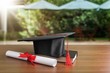 Graduation hat and diploma on wooden background