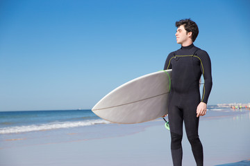 Smiling handsome young man holding surfboard on sunny beach