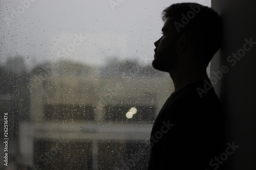 silhouette of a man sitting in the window with rain in mood of sadness and depression