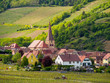 Wide view of the pariah crooked spire church of St. Gall and medieval houses of the valley village of Niedermorschwihr. Haut-Rhin, France. Travel and tourism.