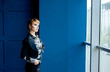 © александр таланцев - a young girl in strict clothes stands near the window and looks out the window