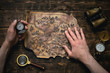 © Dmitriy - Old map in man adventurer hands on a brown table background. Treasure hunt concept.