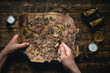 © Dmitriy - Old map in man adventurer hands on a brown table background. Treasure hunt concept.