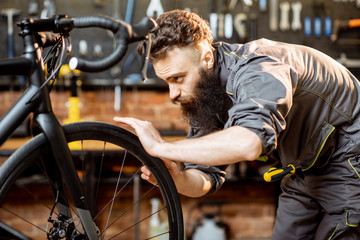 Wall Mural - Handsome bearded repairman in workwear serving a sports bike at the bicycle workshop