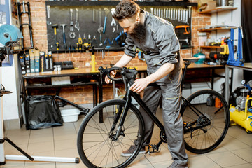 Wall Mural - Handsome bearded repairman in workwear serving a sports bike at the bicycle workshop