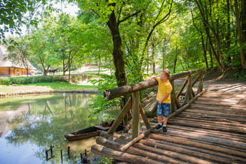  little boy walking near village lake on wooden bridge