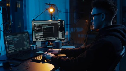 cybercrime, hacking and technology concept - asian male hacker in glasses using computer for cyber attack in dark room at night
