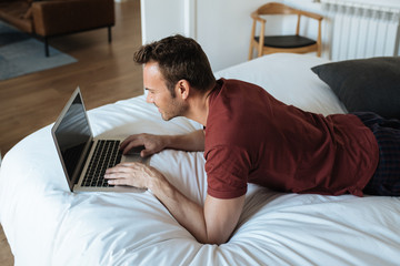 Wall Mural - Man lying down on bed with a computer