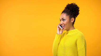 Beautiful young woman talking smartphone on orange background, conversation