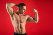 © Alexandr - handsome young man in athletic form on red background shows his muscles