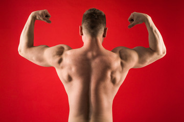 Wall Mural - handsome young man in sports athletic form stands on his back against a red background