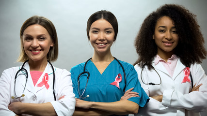 Confident nurses with pink ribbons smiling into camera, breast cancer awareness