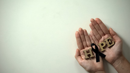 Wall Mural - Woman hands showing black ribbon to camera, melanoma awareness, skin cancer