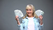 © motortion - Smiling senior woman showing dollar banknotes, quick loan service, banking