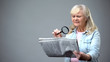 © motortion - Elderly lady trying to read newspaper with magnifying glass, poor vision problem