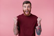 © timtimphoto - Close up of bearded young man with tattooed hand, screaming and cheering for his favorite team, looking at camera isolated over pink background. People and emotion concept.