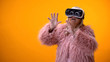 © motortion - Senior woman in funny coat and VR headset playing video game, hi-end innovations