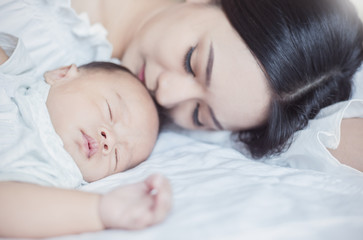 Wall Mural - Closeup portrait of beautiful young asian mother kissing sleeping newborn baby on hospital bed. Healthcare medical family love lifestyle breastfeeding nursery mother’s day together concept