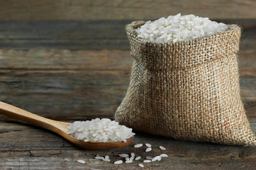 turkish raw white rice grains with burlap sack in wooden spoon on rustic wooden background, healthy food uncooked legumes concept