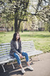 © Bougie Banana - Cheerful asian young woman sitting on a bench under the blooming trees in a park