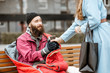 Woman helping homeless beggar giving some hot drink outdoors. Concept of helping poor people