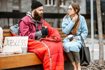 Homeless beggar with young woman listening to his sad story while sitting together on the bench outdoors. Concept of a human understanding