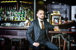 © Vladimir - serious man in a stylish suit drinking whiskey in a pub. Stylish handsome male in an elegant suit holds a glass of whiskey at bar counter background.