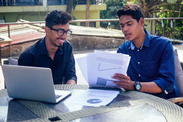 Indian young business people businessman freelancer working outdoors chaise lounge on the beach with laptop.two successful friends freelancing surfing remote work summer vacation in tropical paradise.