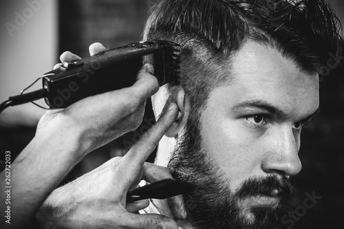 Foto Young handsome barber making haircut for attractive bearded man at barbershop