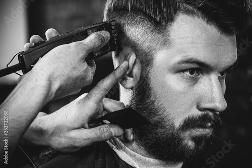 Young handsome barber making haircut for attractive bearded man at barbershop Canvas Print