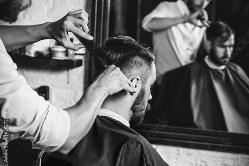 Young handsome barber making haircut for attractive bearded man at barbershop Canvas