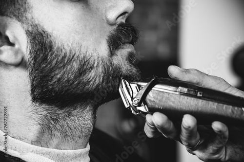 Cuadros en Lienzo Young handsome barber making haircut for attractive bearded man at barbershop
