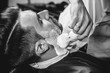 © master1305 - Client during beard shaving in barbershop. Young handsome barber and attractive bearded man. Black and white or colorless photo. Hairstyle, salon, hairdresser, barber shop, lifestyle concept