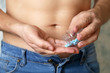 Man taking pills, bottle with blue tablets in male hands close up. Guy in unzipped jeans with naked torso, concept of viagra, drugs for digestion, medication for erection before sex, sleeping pill