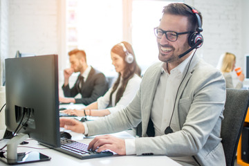 Wall Mural - Cheerful friendly online technical operator agent with headphones and microphone talking with client in customer support office