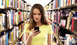 © Syda Productions - technology, cyberbullying and education concept - young woman or teenage girl in blank yellow t-shirt using smartphone over book shelves in library background