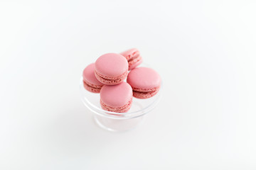 sweets, pastry and food concept - pink macarons on glass confectionery stand over white background