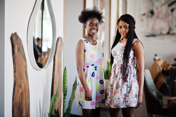 Two black african girlfriends at summer dresses posed in cafe.