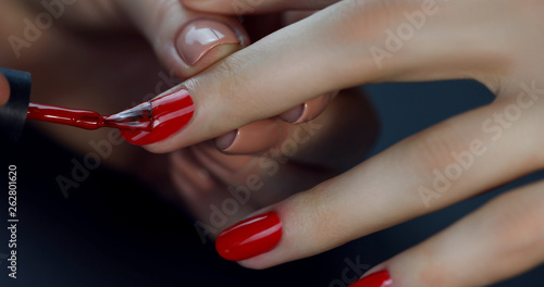 the manicurist paints the client's nails with red nail polish on a black background  Painting nails Fototapet
